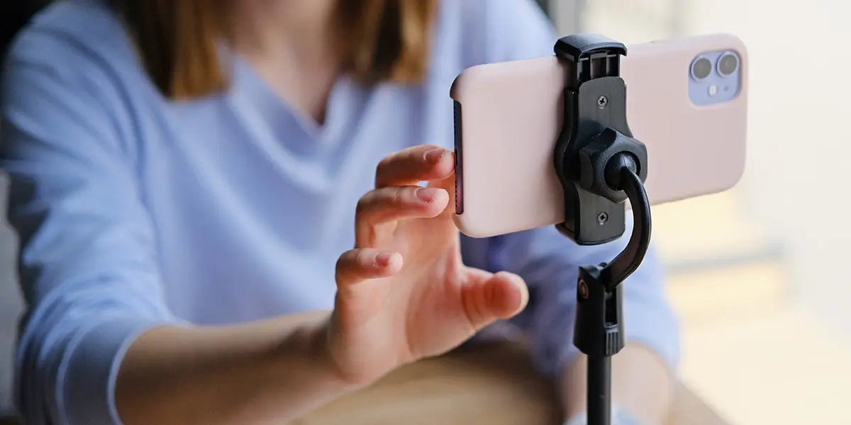 Remote Video image is of a person using her phone on a stand to record a video.