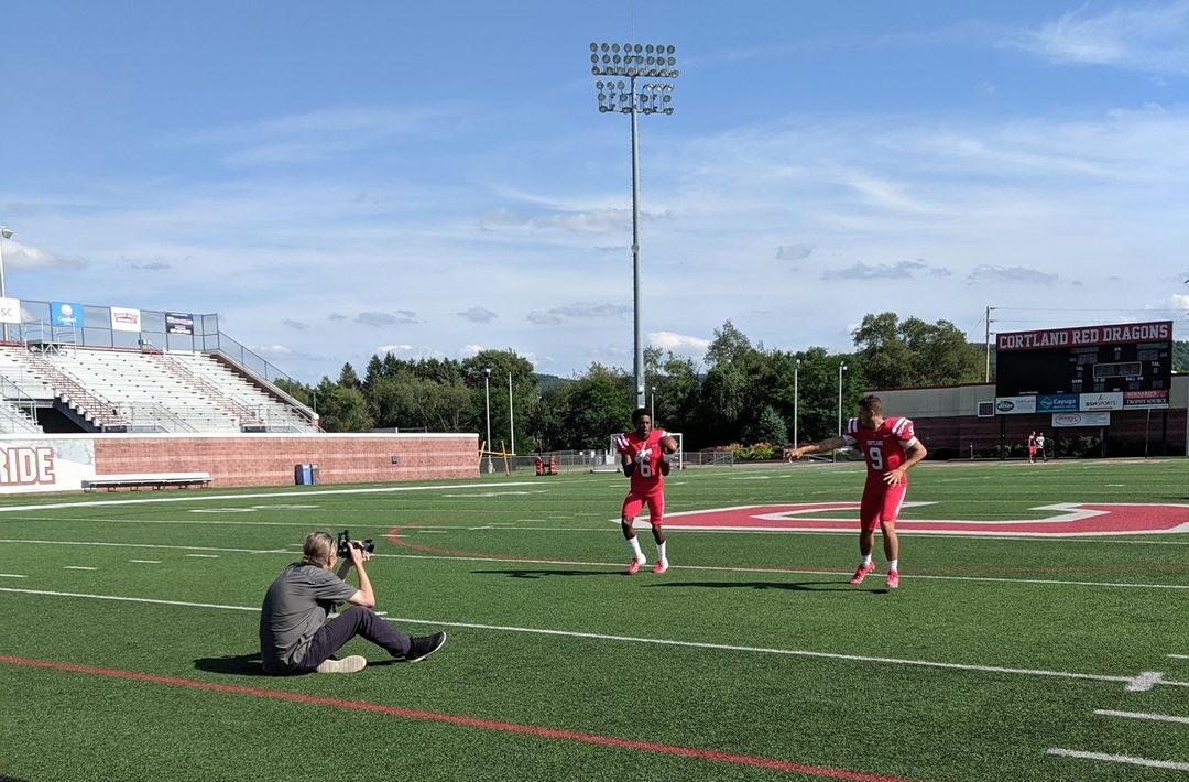 Videographer filming two football players in SUNY Cortland's stadium.
