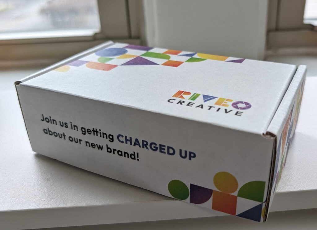 Box with Riveo Creative branding and text that says "Join us in getting CHARGED UP about our new brand!".